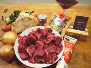 Ein Teller mit rohem Gulaschwürfeln. Rundherum weitere Zutaten.