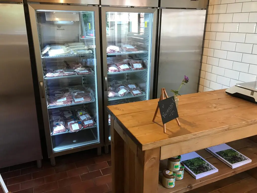 Verkaufstresen aus Holz mit kleiner Standtafel "Reserviert". Im Hintergrund volle Kühlschränke mit dem vakuumierten Fleisch.